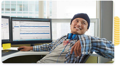 An employee sitting behind two monitors, leaning back and smiling