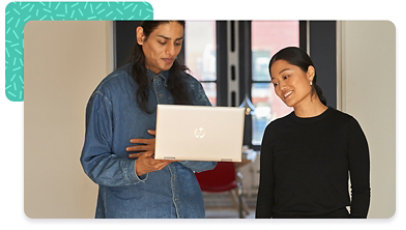 Two colleagues standing next to one another, both looking at a laptop one is holding up
