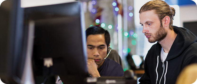שני גברים מתמקדים במסך מחשב בסביבה משרדית מודרנית, אחד אסייתי ואחד לבן