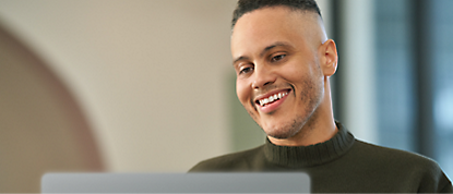 男性がノート PC を使用しながら微笑んでいます。