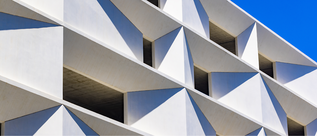 Abstract view of a modern building with geometric white concrete facade under a clear blue sky.