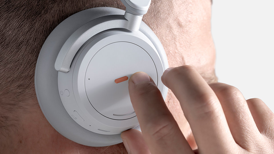 Die Hände einer Person berühren einen Aufkleber für das adaptive Surface-Kit am Ohrpolster von Surface Headphones.