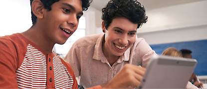 Dois jovens sorriem enquanto utilizam um tablet.