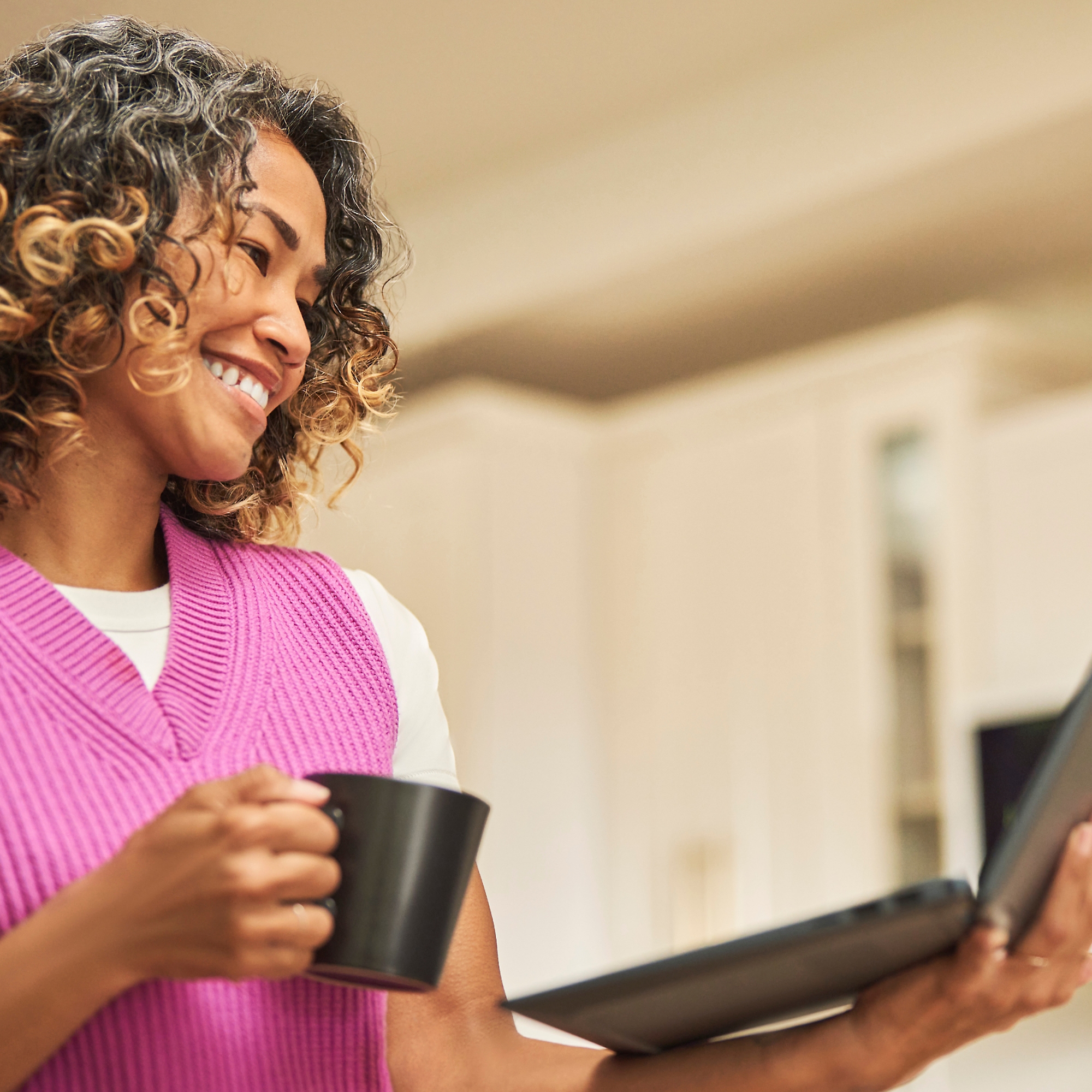 Hymyilevä nainen, jolla on kahvikuppi toisessa kädessään ja kannettava tietokone toisessa
