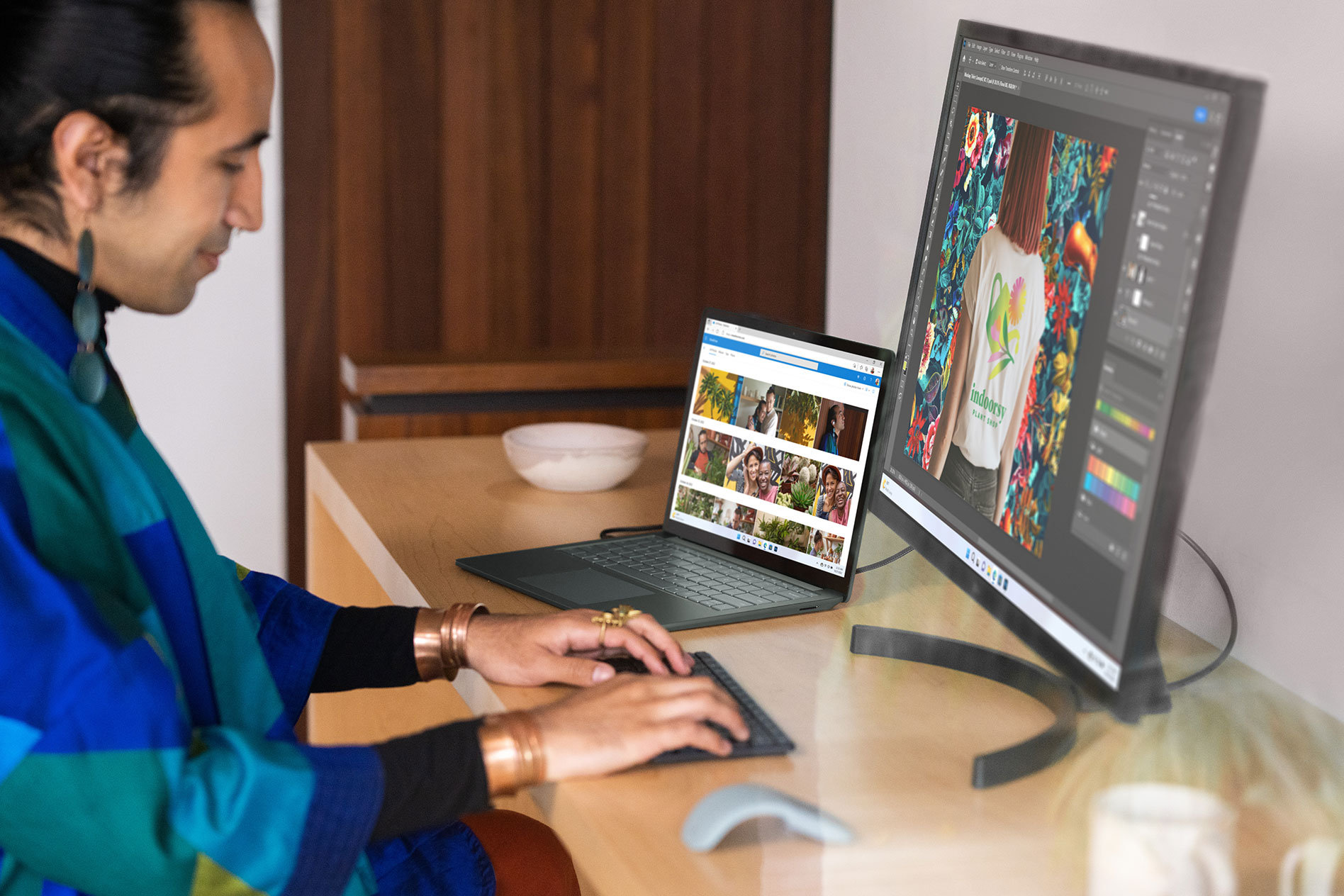 Ein Mensch sitzt an einem Holztisch und tippt auf einer externen Tastatur, während das Surface Laptop 5 und ein externer Monitor Fotos auf dem Bildschirm anzeigen.