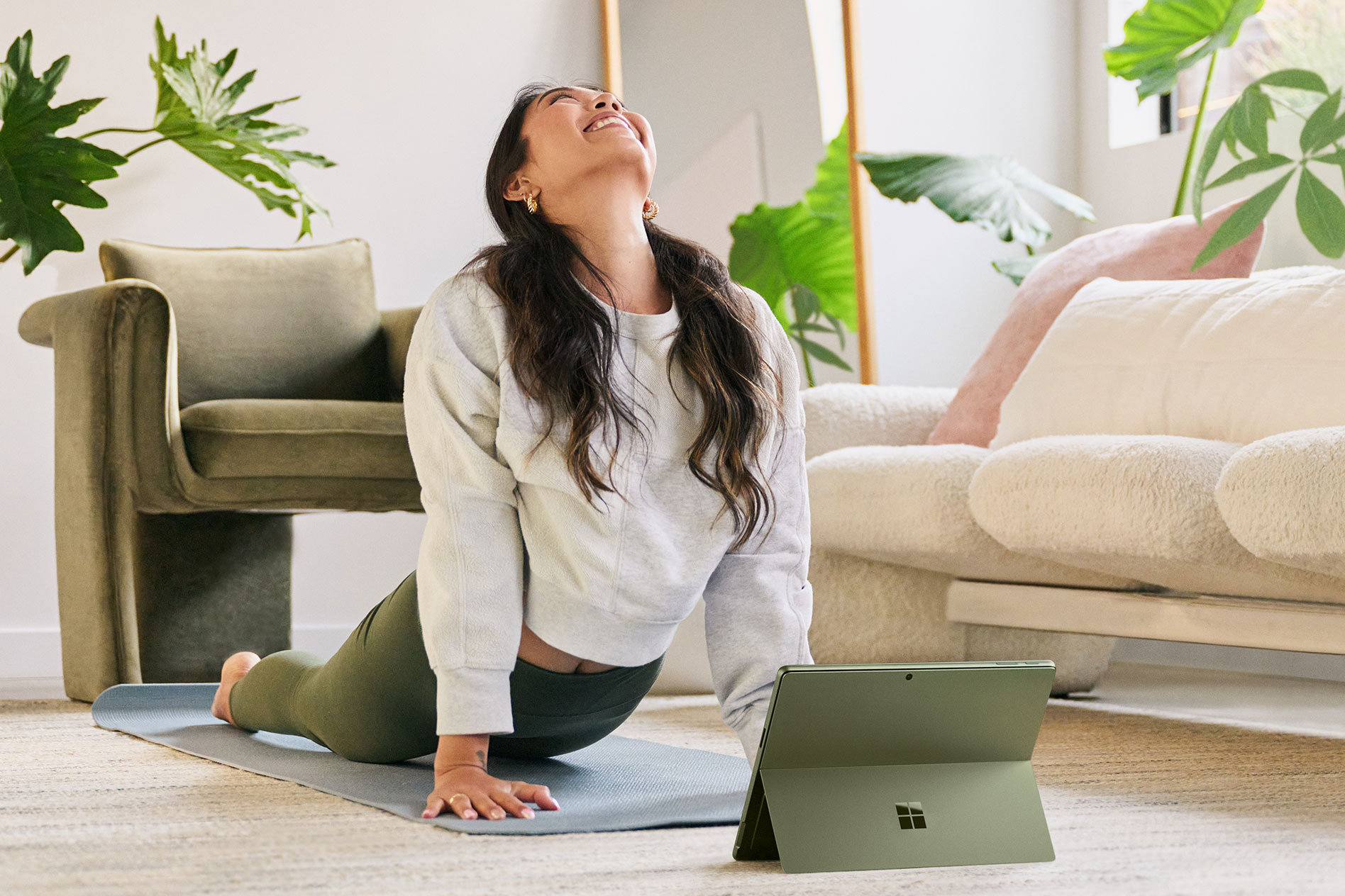 Seorang wanita melakukan gaya yoga di atas lantai ruang tamu dengan Surface Pro 9 miliknya terus di hadapannya.