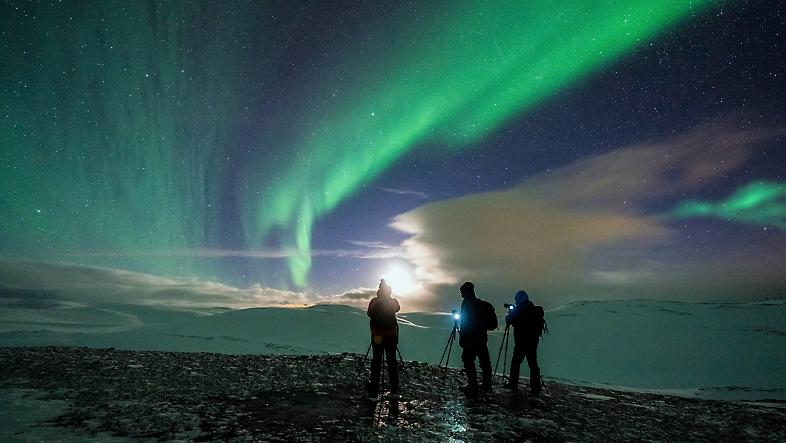 三个人将相机架在三脚架上拍摄北极光。
