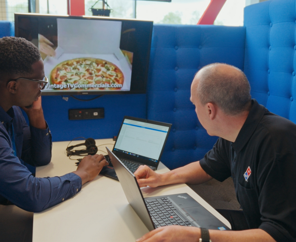 Δύο άτομα κάθονται με φορητό υπολογιστή και συζητούν για την πίτσα Dominos