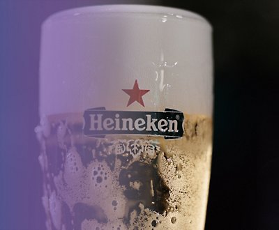 紫と黒の背景に Heineken ビールのグラス。