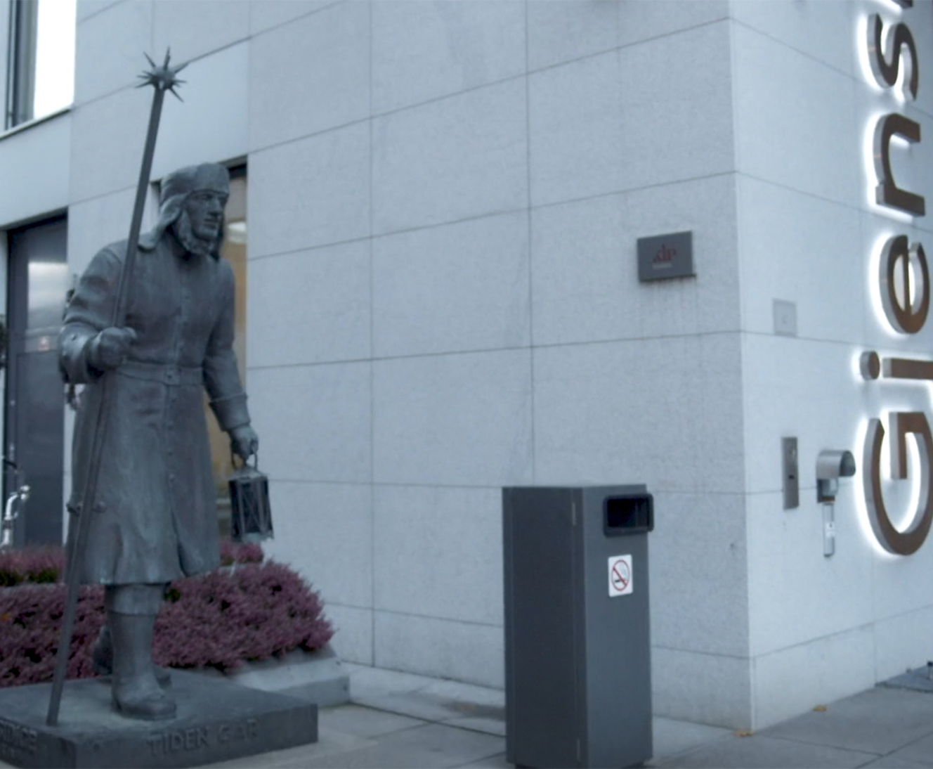 A statue of a person holding a staff near a building where Giensidge is written vertically.