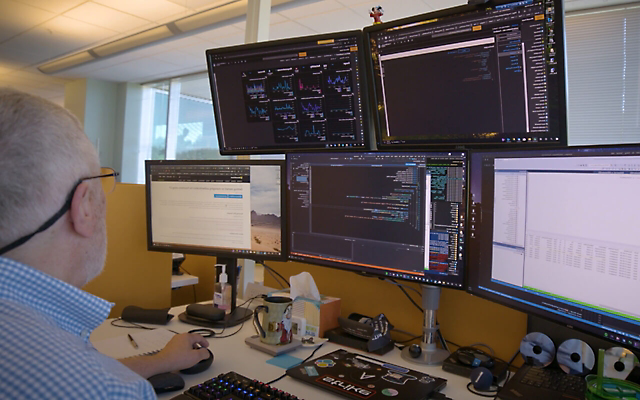 Uma pessoa trabalhando em sua mesa com cinco telas exibindo dados e aplicativos