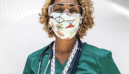 Een zorgprofessional die scrubs, een stethoscoop, een veiligheidsbril en een masker draagt.