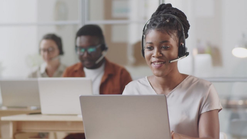 Žena nosi slušalice sa mikrofonom dok radi za laptopom.