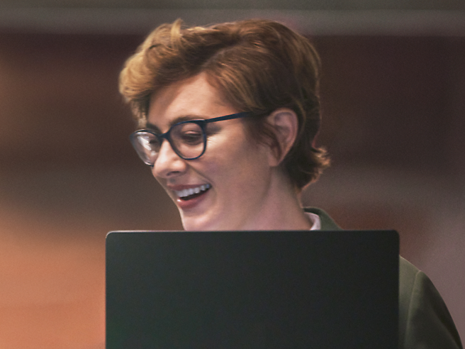Eine lächelnde Frau mit Brille arbeitet an einem Laptop