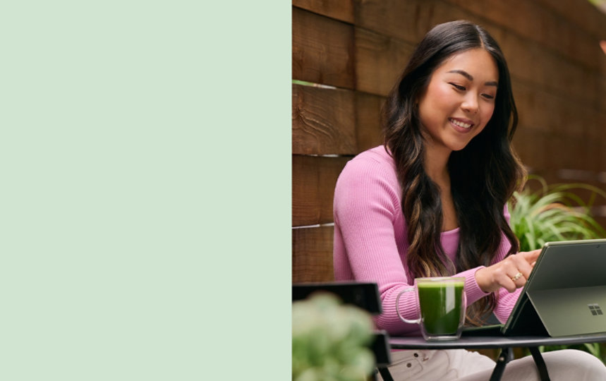 一位女士使用她的仙茶绿 Surface Pro 9 在外面工作
