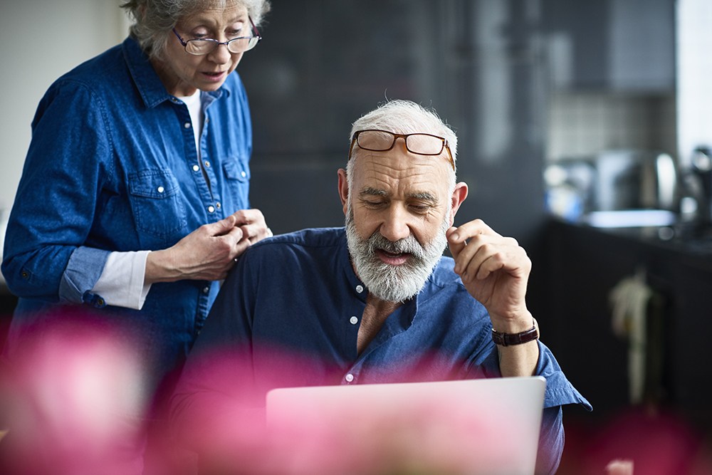 white man with white beard and denim shirt talking with woman over laptop