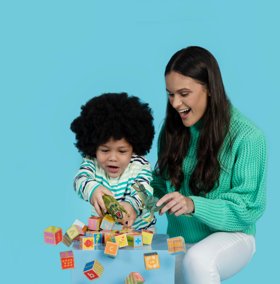 Babysitter and child smiling while playing with dinosaurs and blocks