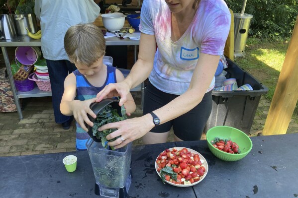 Grow It organizer Leah Reichardt-Osterkatz, right, helps children make smoothies from strawberries they picked, plus kale grown on the farm, at Spring Forest in Hillsborough, N.C., on Wednesday, May 29, 2024. (Yonat Shimron/Religion News Service via AP)