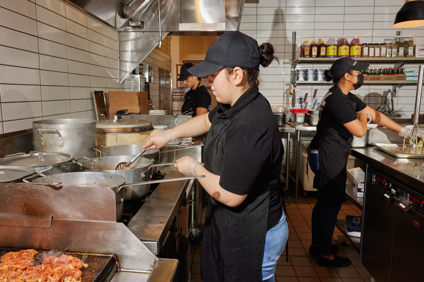 A Chipotle worker stirs beans cooking on the stove on the left while another peels avocados for guacamole on the right, at the Chipotle restaurant in Corona Del Mar, California.