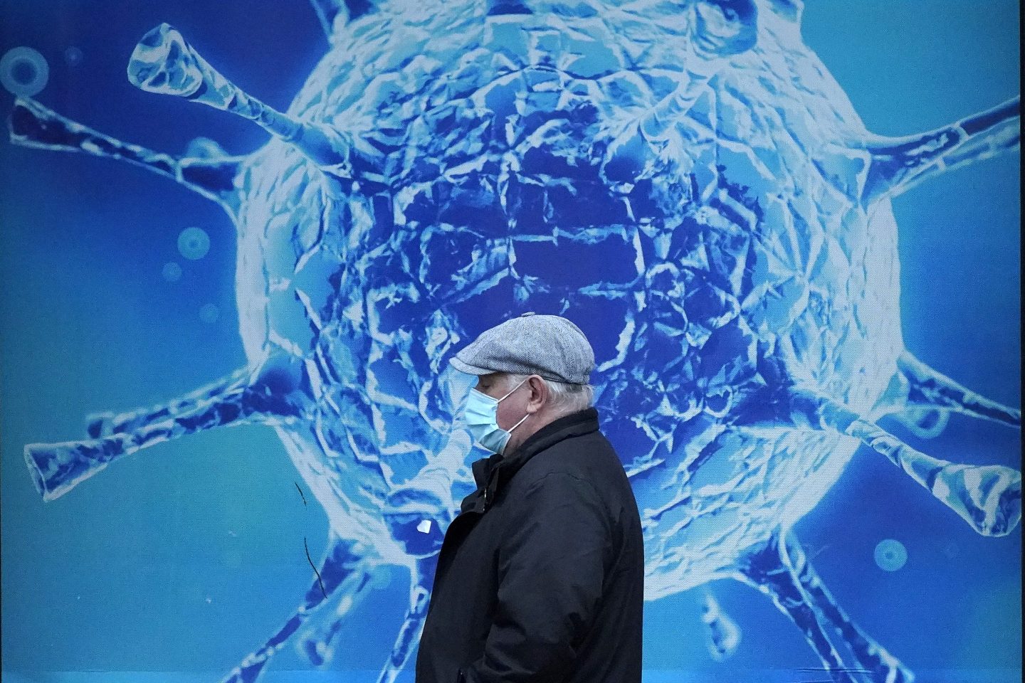 OLDHAM, UNITED KINGDOM &#8211; NOVEMBER 24: A man wearing a protective face mask walks past an illustration of a virus outside Oldham Regional Science Centre on November 24, 2020 in Oldham, United Kingdom. England is continuing its second national coronavirus lockdown. People are still permitted to exercise with one other person, takeaway food is permitted but bars and restaurants are shut for sit-in service. Schools will remain open but people are being advised to work from home where possible and only undertake necessary travel. All non-essential shops are closed with supermarkets and builders&#8217; merchants remaining open. (Photo by Christopher Furlong/Getty Images)