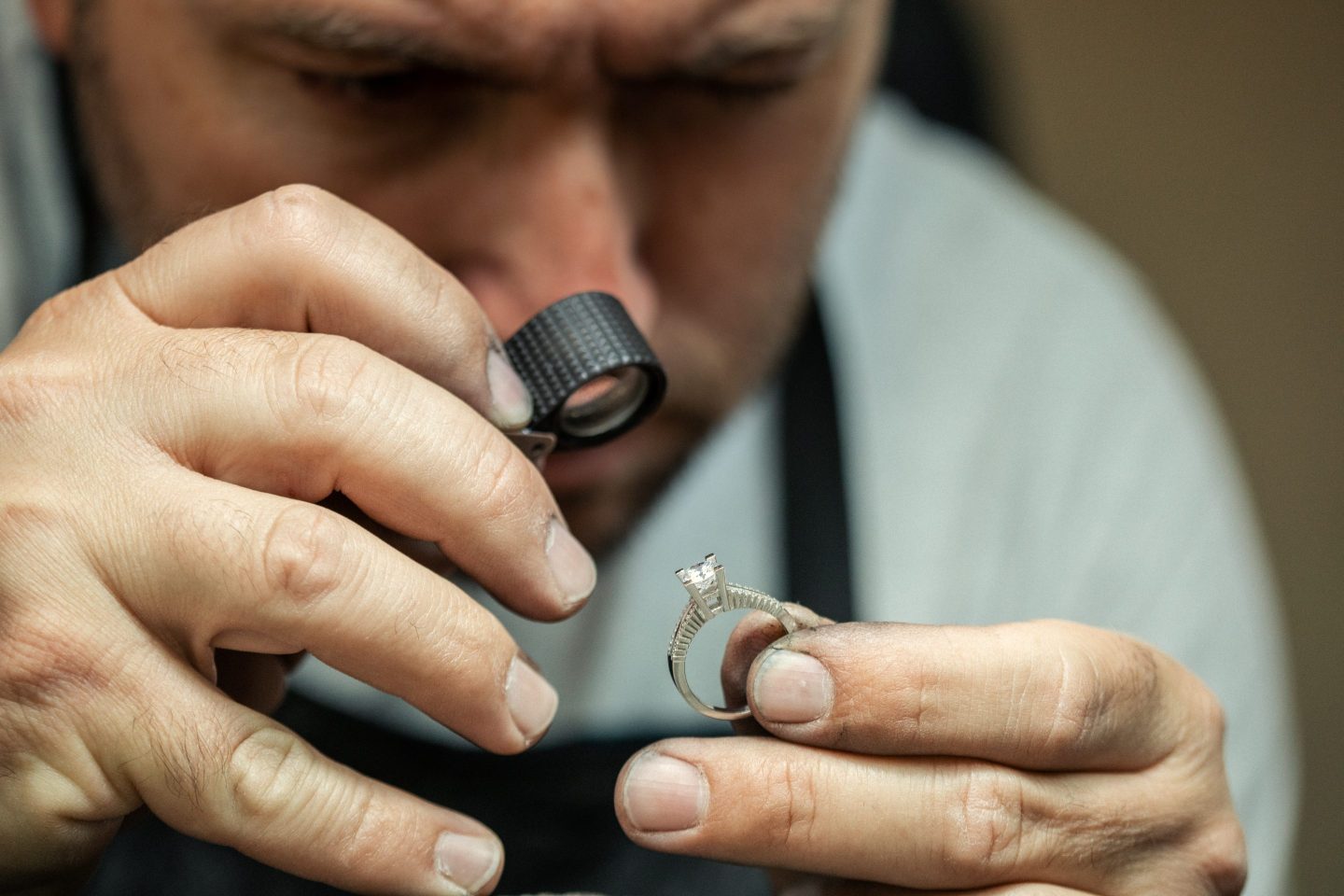 A man looks through a magnifier at a diamond set in a ring.