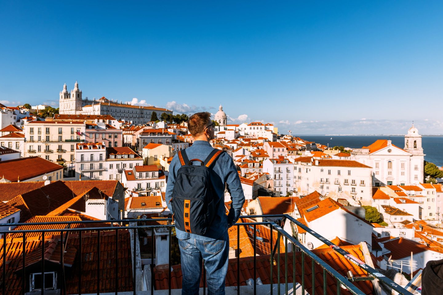 Man with backpack looking at Lisbon old town cityscape from a scenic viewpoint (miradouro), Portugal