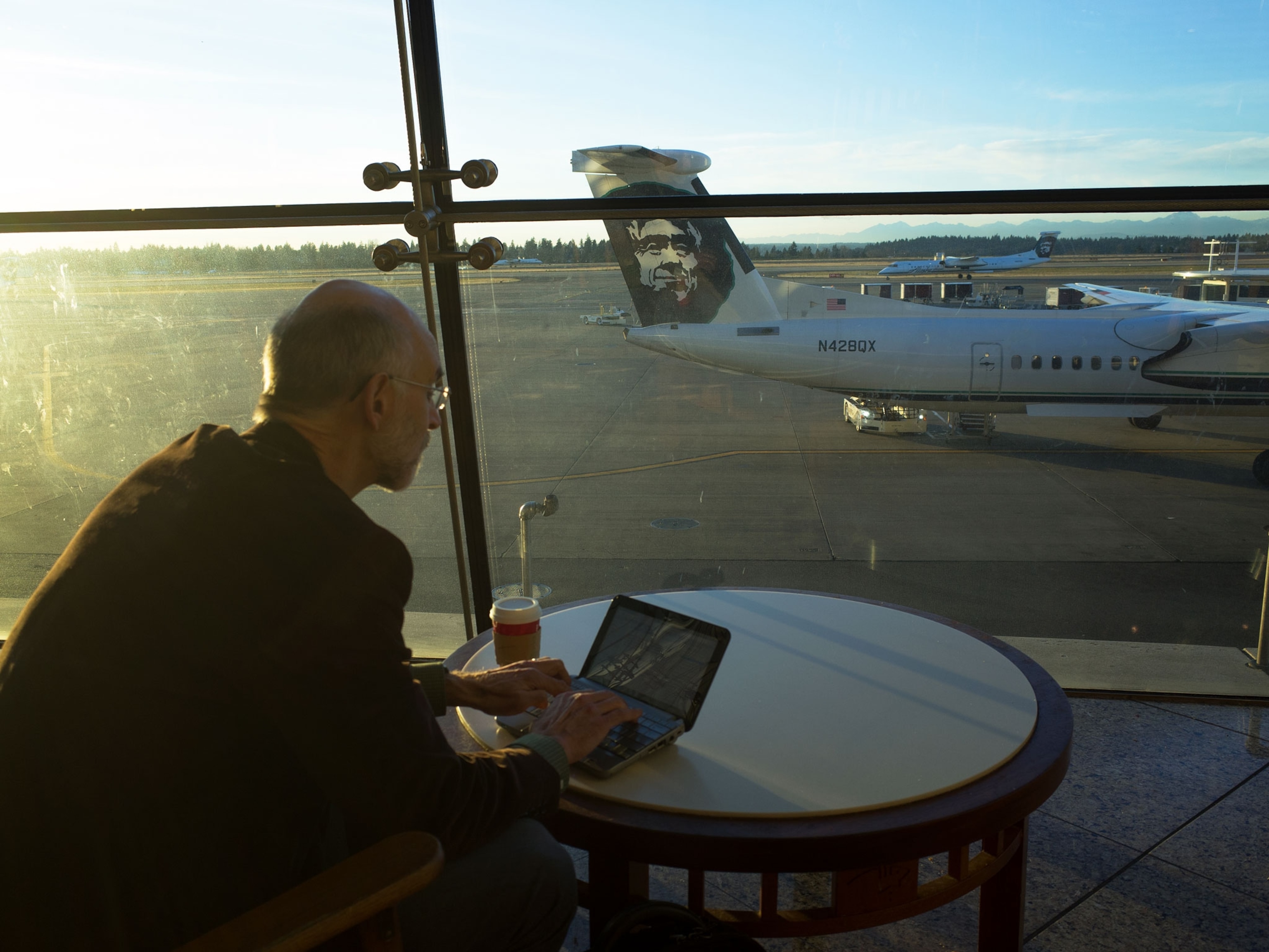 a man on a computer in an airport terminal looking out at a plane