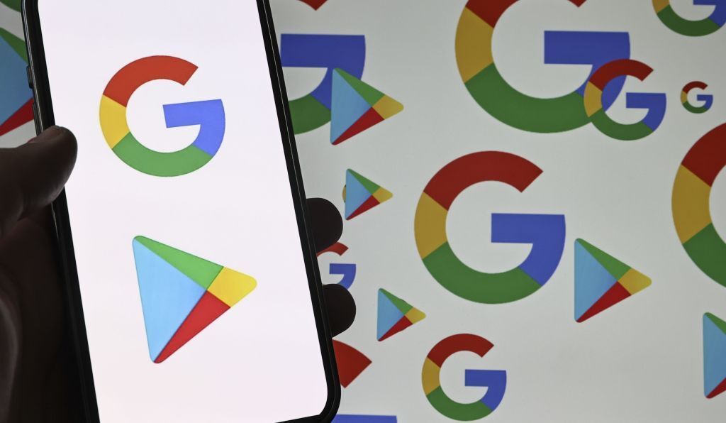 The Google Play and Google logos as seen on a phone's screen, wih the same logos visible in the background