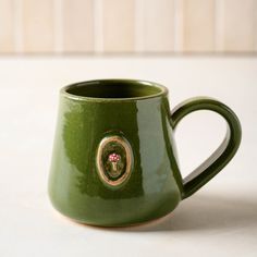 a green coffee mug with a gold emblem on it