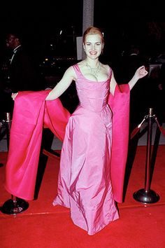 a woman in a pink dress standing on a red carpet with her arms spread out