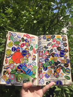 a hand holding an open notebook with stickers on it and trees in the background