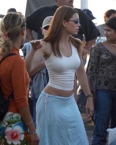 a woman in white top and blue skirt standing next to other people at an outdoor event