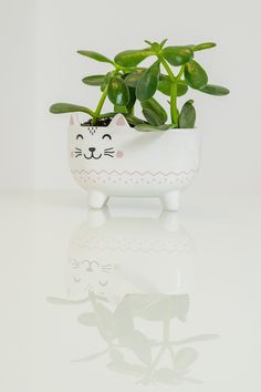 a white cat planter with green plants in it