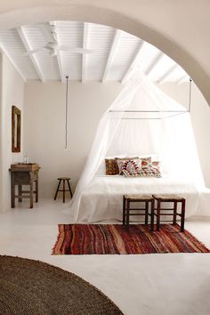 a bed sitting under a white canopy next to a wooden table and chair on top of a rug