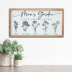 a wooden framed sign that says mom's garden, love grows here and three potted plants