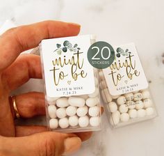 two small white candy bags with wedding favors in them, one being held by someone's hand