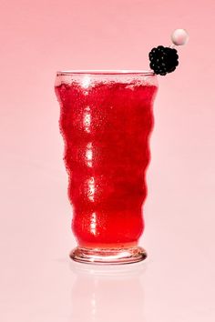 a red drink in a glass with a black cherry on the top and a white ball sticking out of it