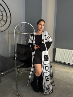 a woman standing in front of a chair wearing black and white crocheted coat