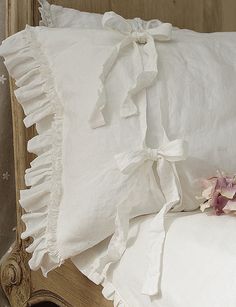a white pillow with ruffled edges and pink flowers on the bottom, sitting on a bed