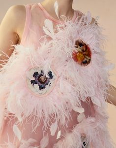 a close up of a woman wearing a pink dress with feathers on it and a heart shaped brooch