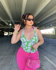 a woman in pink pants and a green top holding a handbag while standing under an overpass