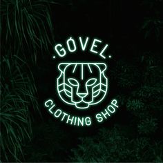 a neon sign that says govel clothing shop in front of some plants and trees