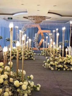 a room filled with lots of white flowers and tall gold candles in the middle of it
