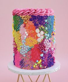 a multicolored cake with sprinkles and beads sits on a stand