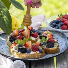 a person is spreading fruit on top of toasted bread with honey and blueberries