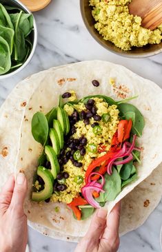 someone holding up a tortilla with black beans, avocado and red onions
