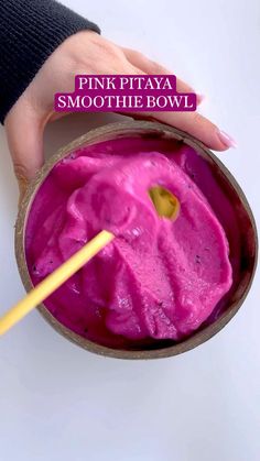 a person holding a spoon in a bowl filled with pink colored liquid and gold spoon