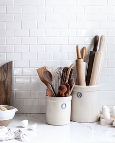 kitchen utensils and wooden spoons in white ceramic containers on counter with white brick wall