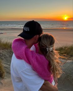 a man and woman hug on the beach at sunset