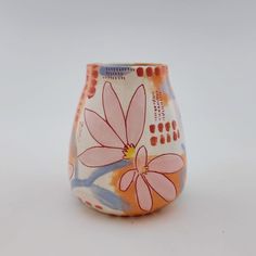 a small vase with flowers painted on it's sides, sitting on a white surface